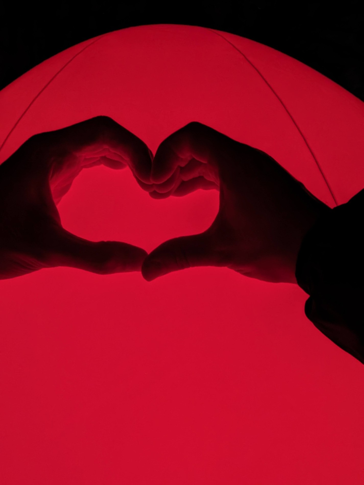 Two hands forming a heart in front of a red circular light